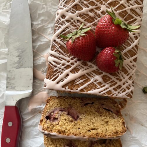 Sourdough strawberry bread partially sliced with fresh strawberries on a parchment paper.