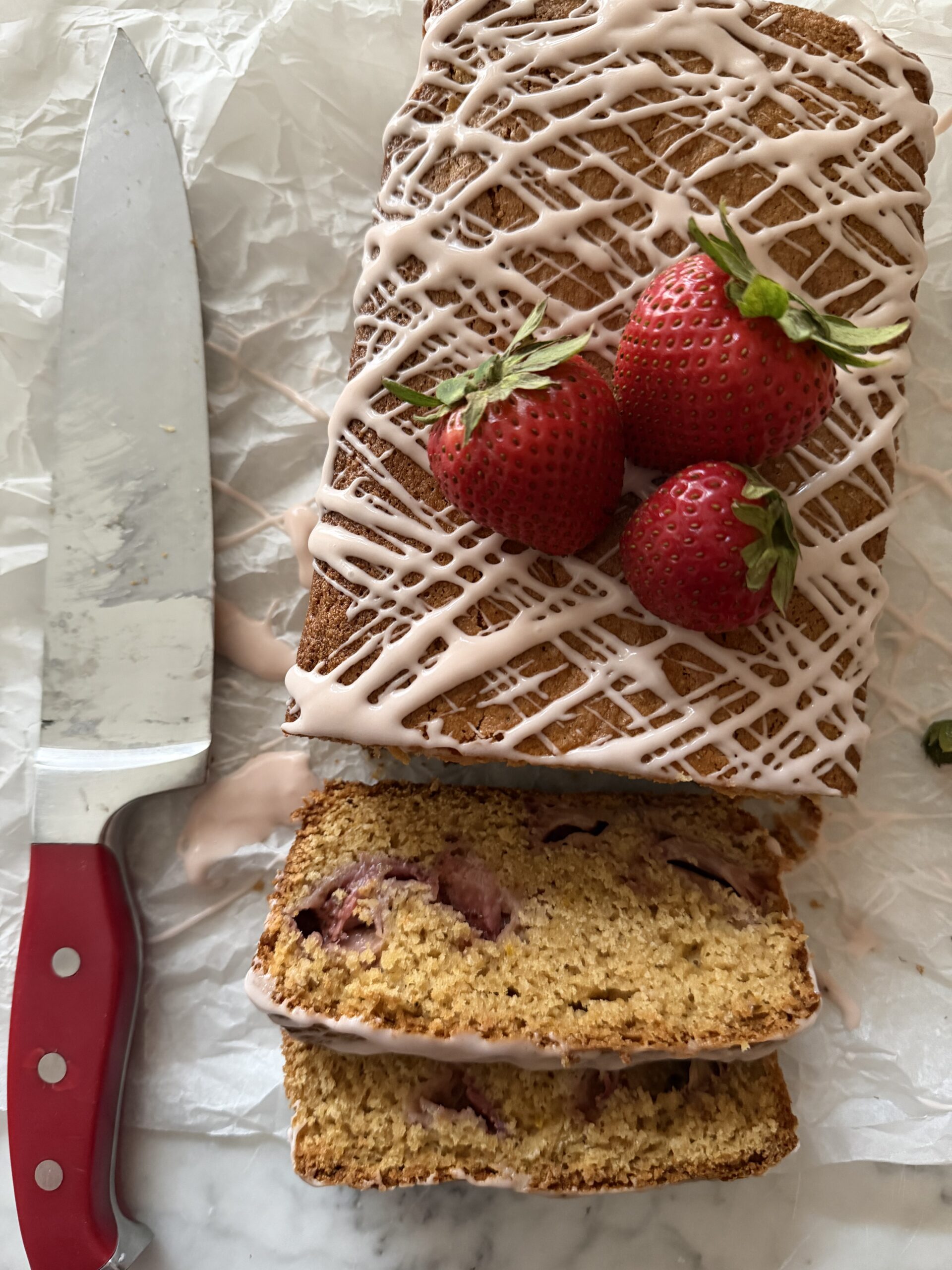 Sourdough strawberry bread partially sliced with fresh strawberries on a parchment paper.