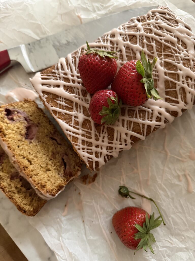 A colorful display of a sourdough strawberry quick bread with strawberry glazing on a wrinkled parchment paper.