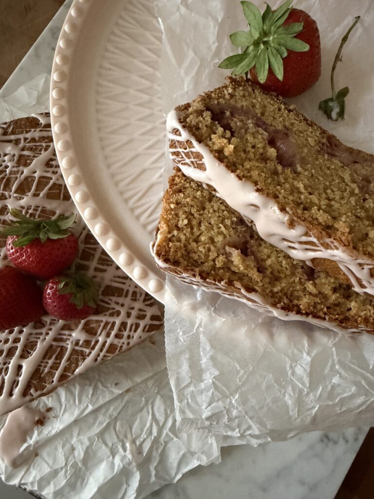 Sourdough Strawberry quick bread slices are sitting on a pink cake stand with the loaf in the background ready to serve to guests. 