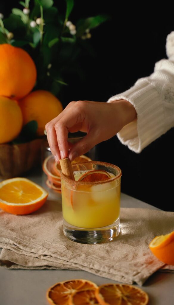 A person garnishes a homemade orange cocktail with a cinnamon stick.
