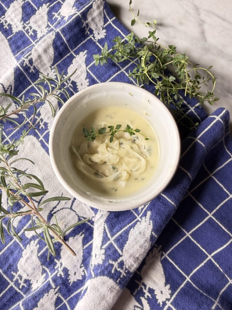 Rosemary Garlic compound butter in a white dish surrounded by fresh herbs. 