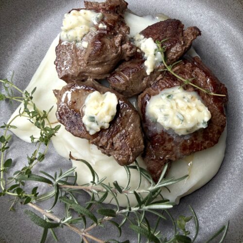 Pan seared venison with savory compound butter over creamy mashed potatoes.