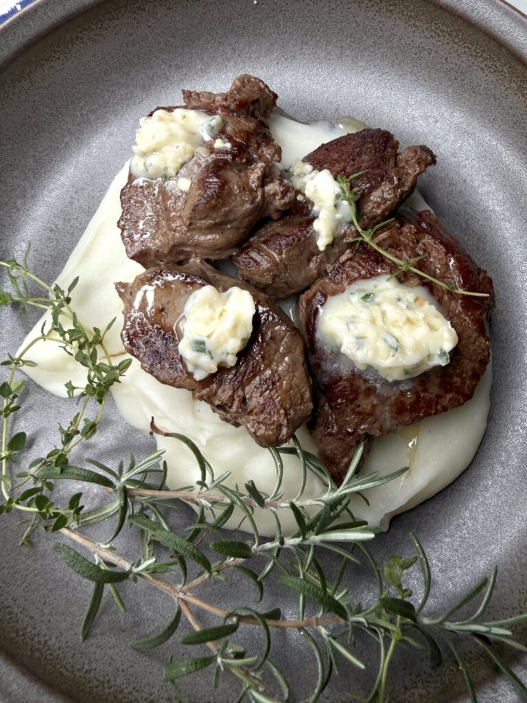 Pan seared venison with savory compound butter over creamy mashed potatoes.