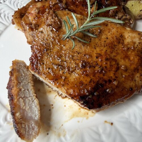 A tender piece of Honey garlic pork chops with fresh rosemary on a white serving platter.