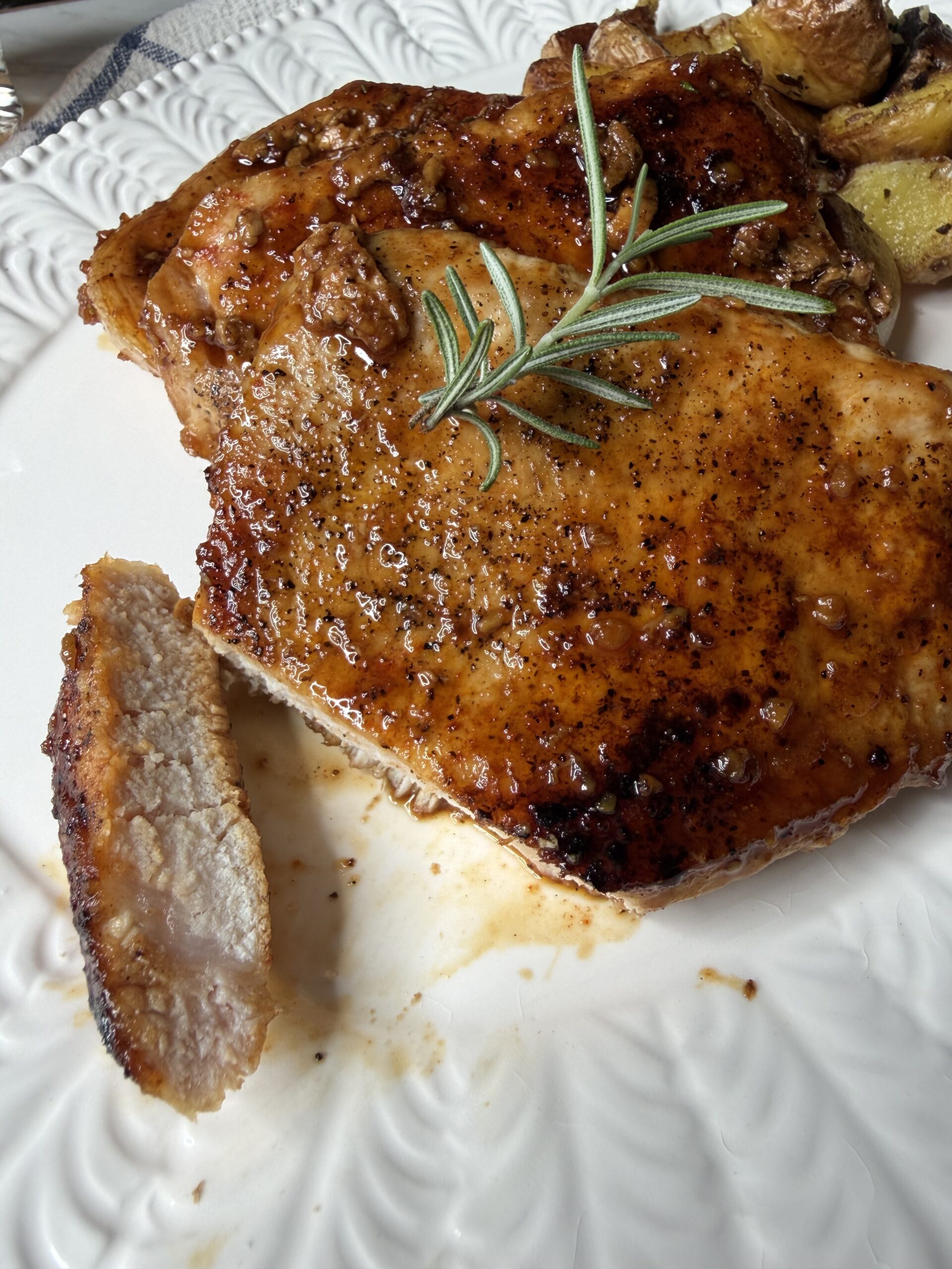 A tender piece of Honey garlic pork chops with fresh rosemary on a white serving platter.