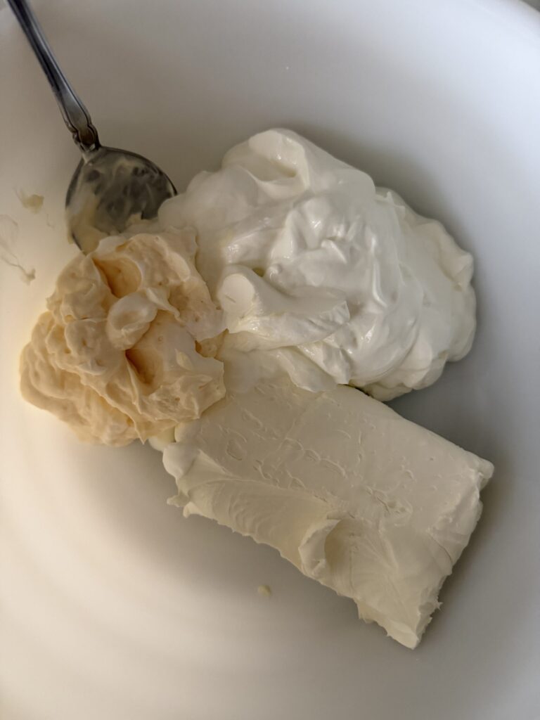 Sour cream, mayonnaise, and cream cheese in a white mixing bowl.