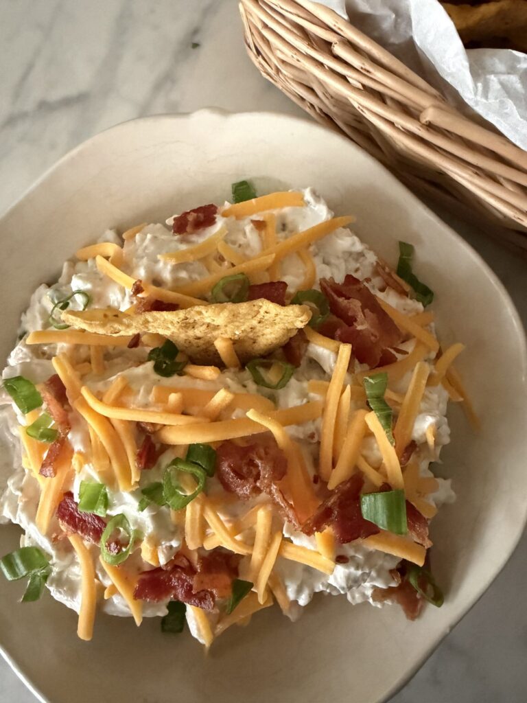 Creamy ranch dip with chicken, bacon, and cheddar cheese in a white bowl.