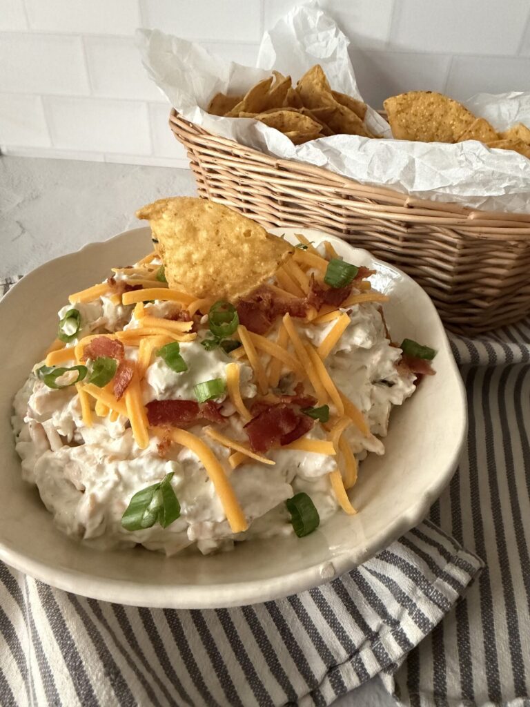A bowl of chicken bacon ranch dip with chips on a striped tea towel.