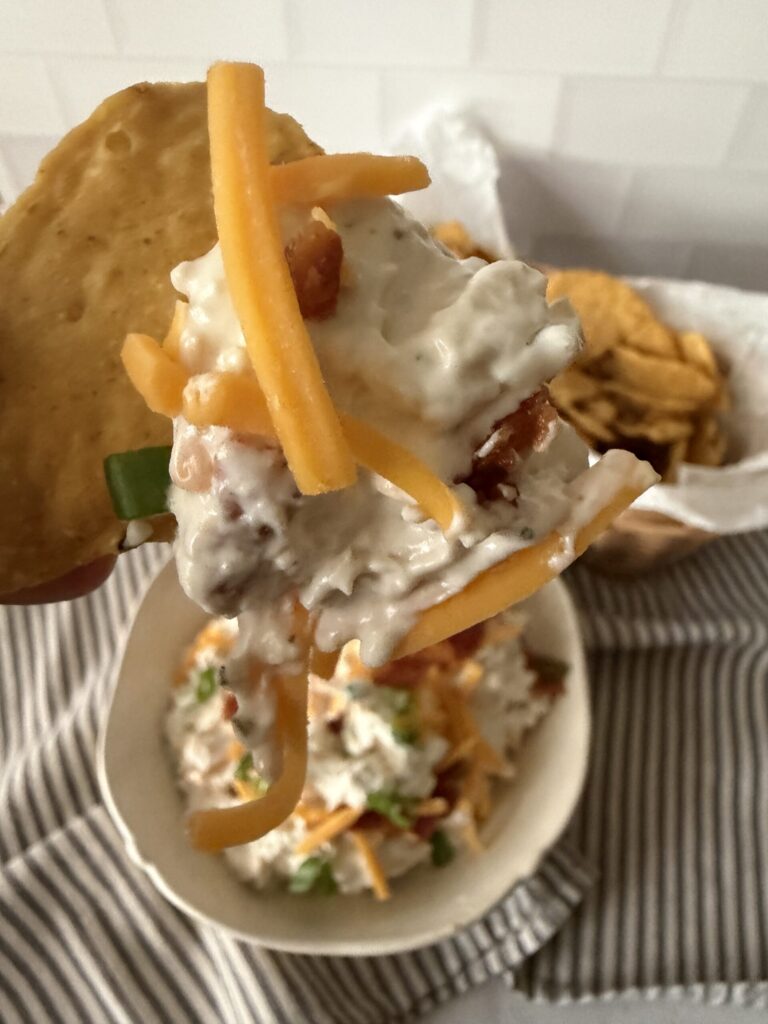 A bite of creamy chicken bacon ranch dip on a chip.