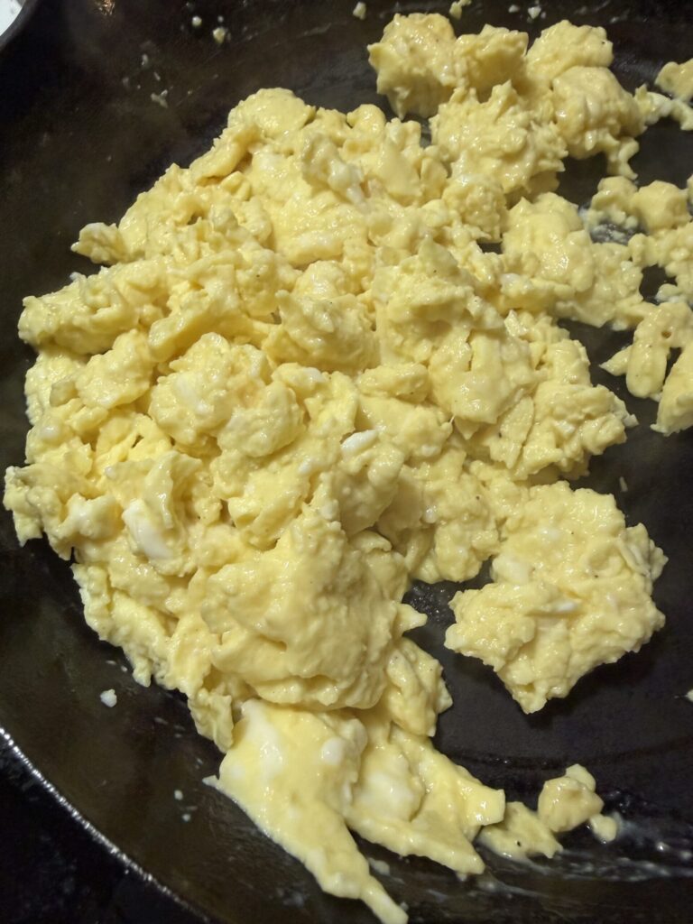 Scrambled eggs are cooking in a cast iron skillet.