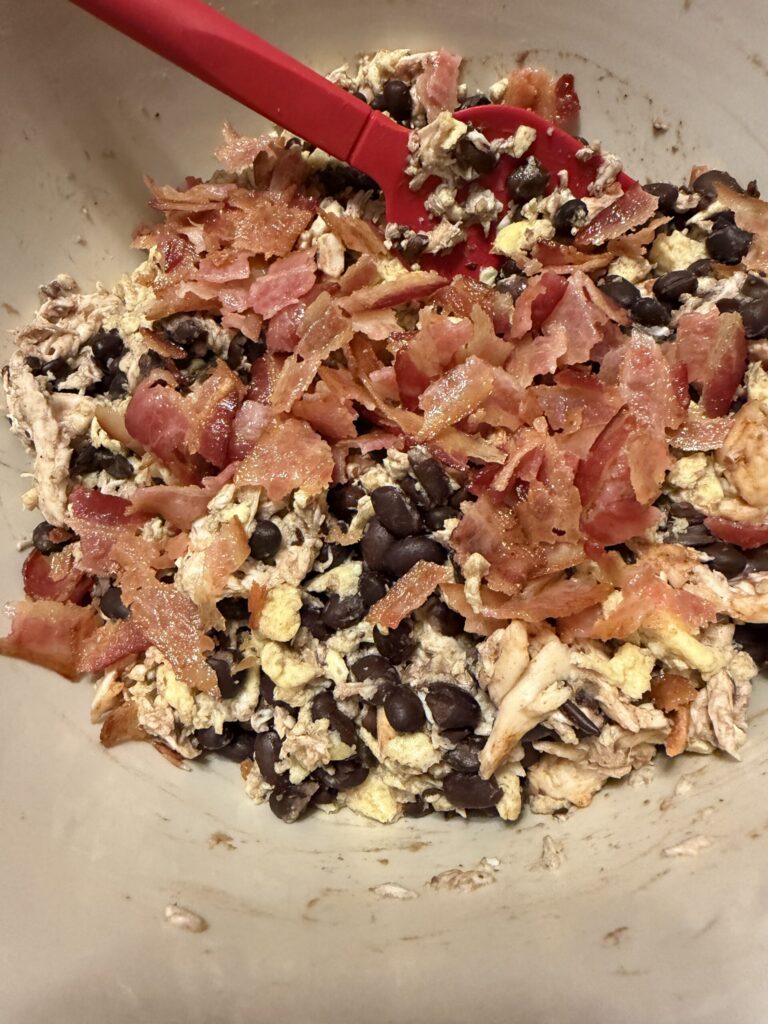 The breakfast burrito filling is mixed together in a bowl with shredded chicken, scrambled eggs, bacon, and cheese.