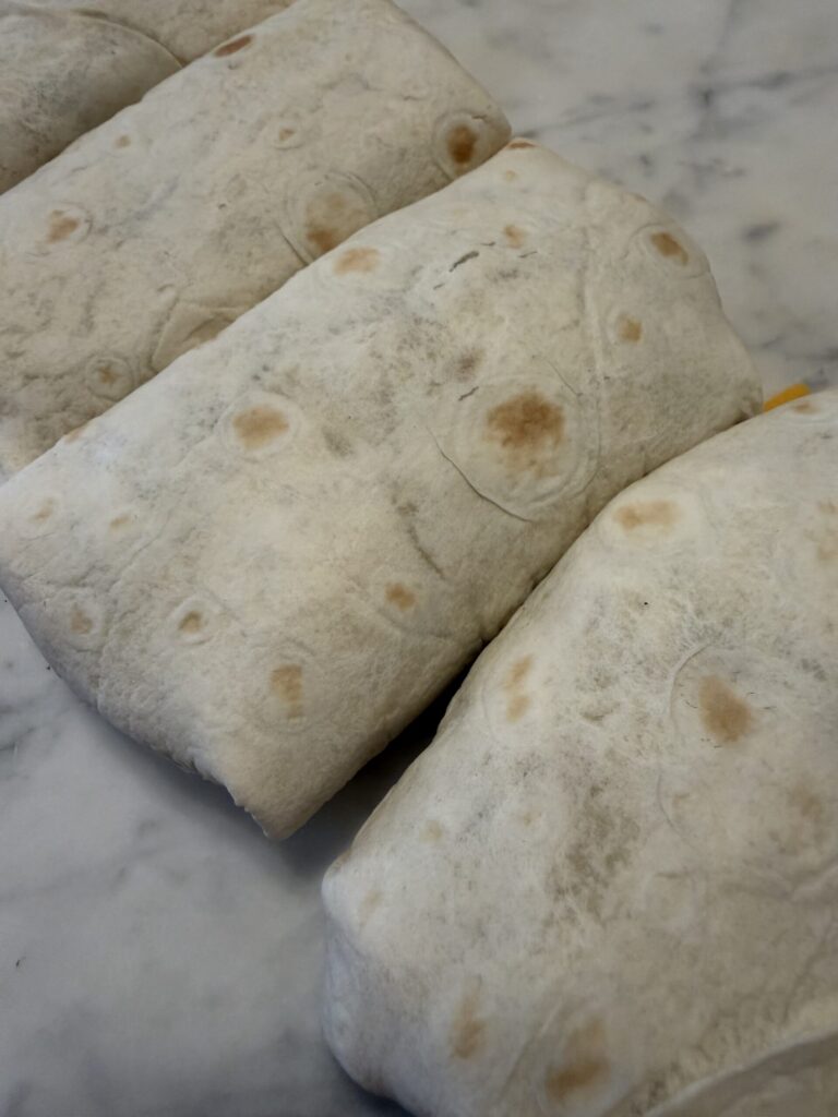 Freshly wrapped breakfast burritos are lined up and ready to be grilled.