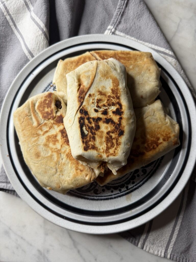 A stack of golden grilled breakfast burritos sits on a decorative plate.