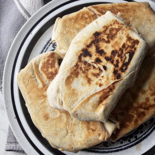 Golden and crisp high protein breakfast burritos in sourdough tortillas on a plate ready to freeze for meal prep.
