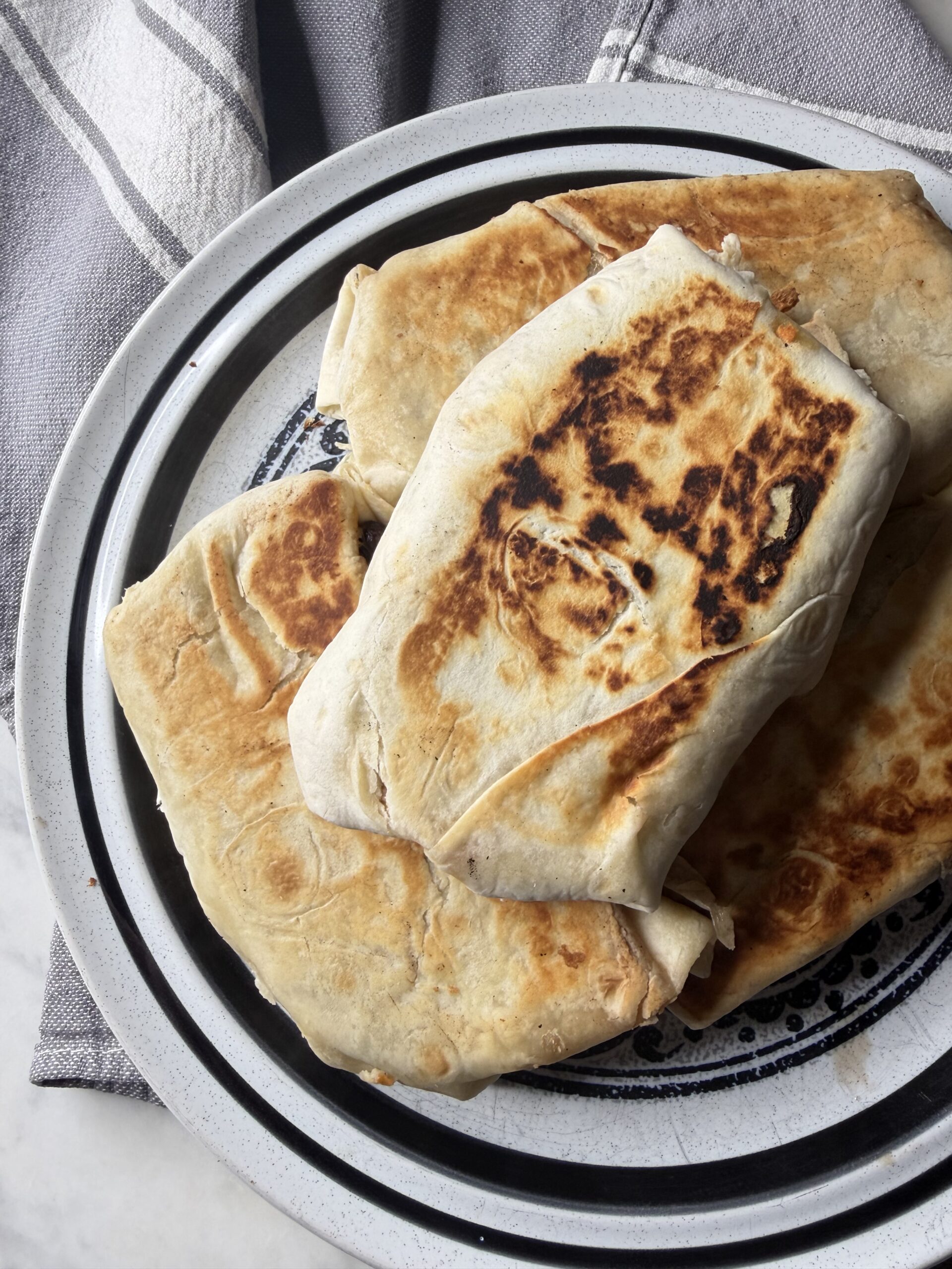 Golden and crisp high protein breakfast burritos in sourdough tortillas on a plate ready to freeze for meal prep.