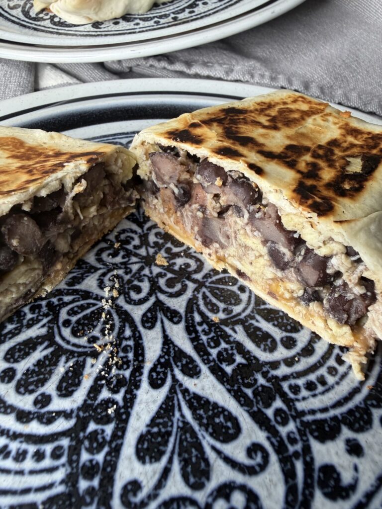A breakfast burrito is cut in half, revealing the chicken, eggs, bacon, and cheese filling.