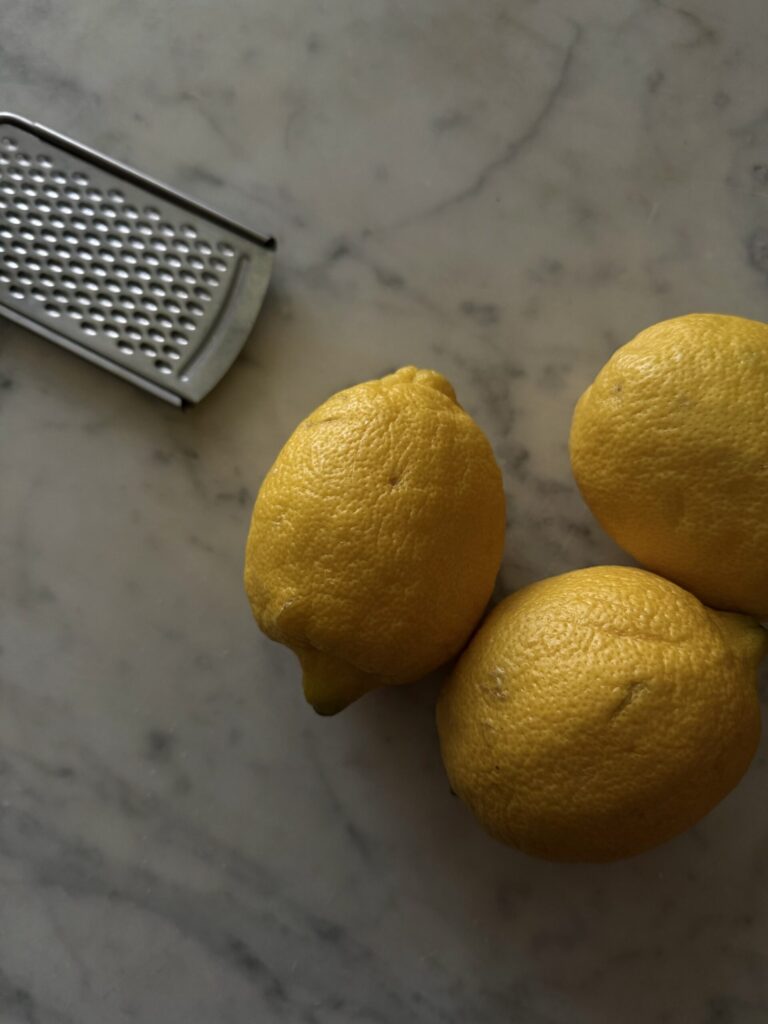 Two large lemons with a zester on a marble surface.