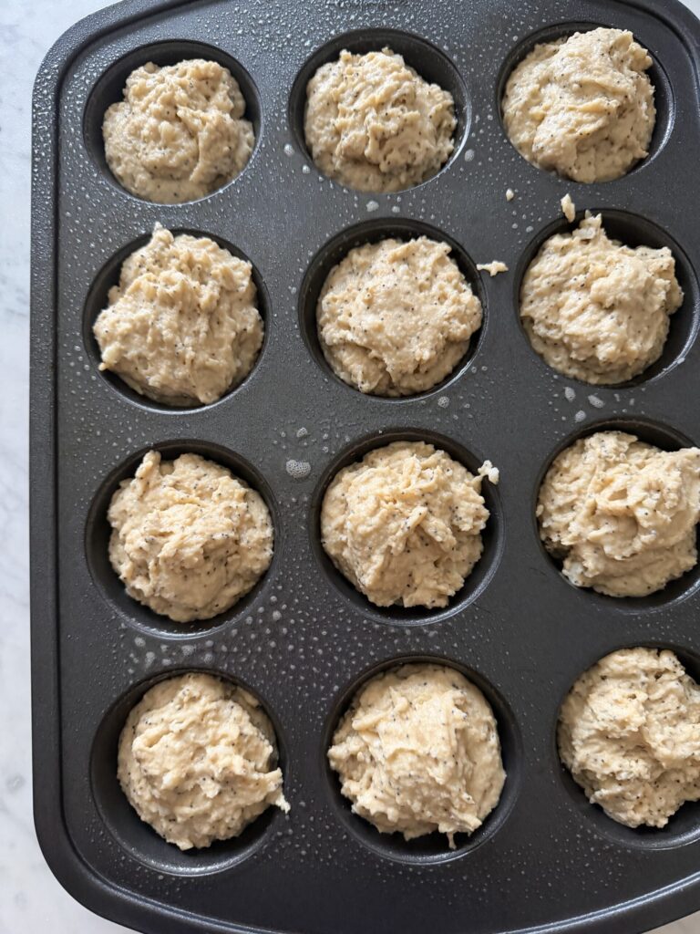 Sourdough poppy seed muffins are scooped in a muffin pan ready to bake.