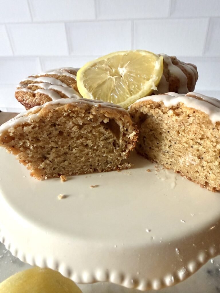 Lemon Poppy Seed muffins with a lemon slice garnish on a glass cake stand.