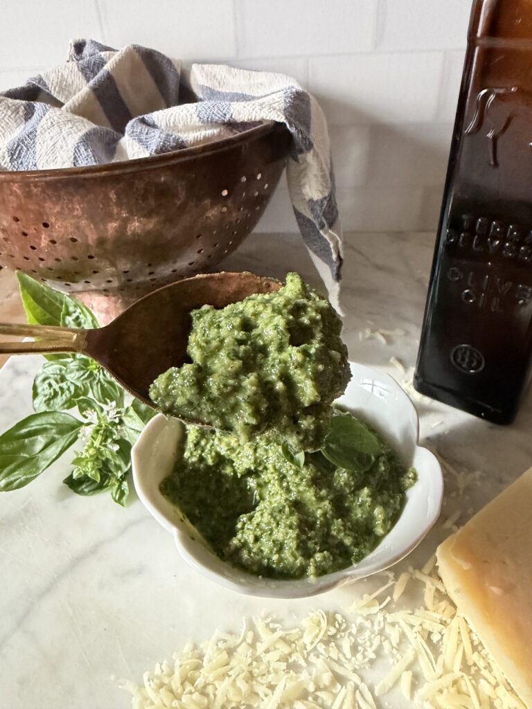 A copper spoonful of homemade pesto over a white bowl.