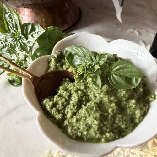 Homemade basil walnut pesto in a white bowl with copper spoon on a marble surface.