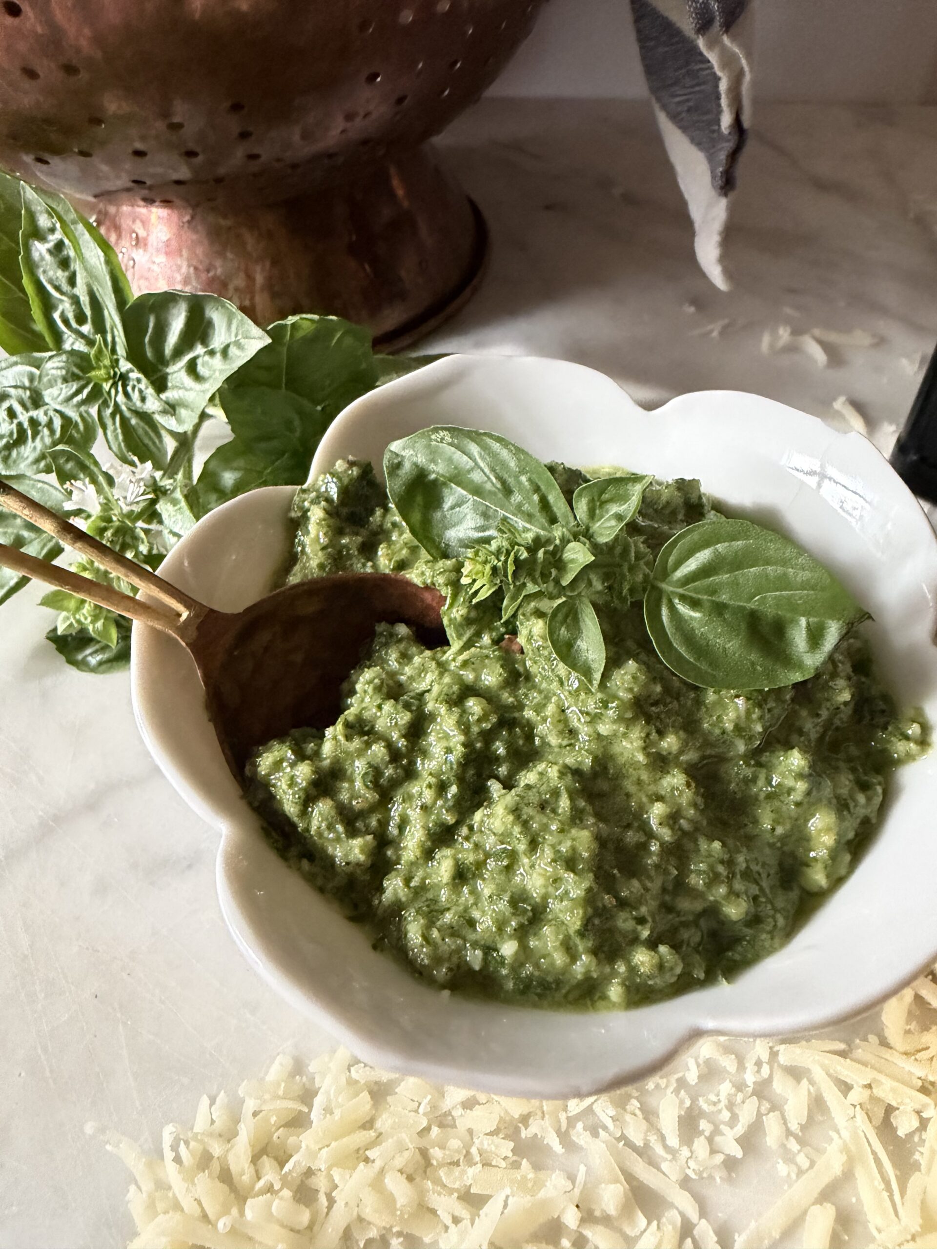 Homemade basil walnut pesto in a white bowl with copper spoon on a marble surface.