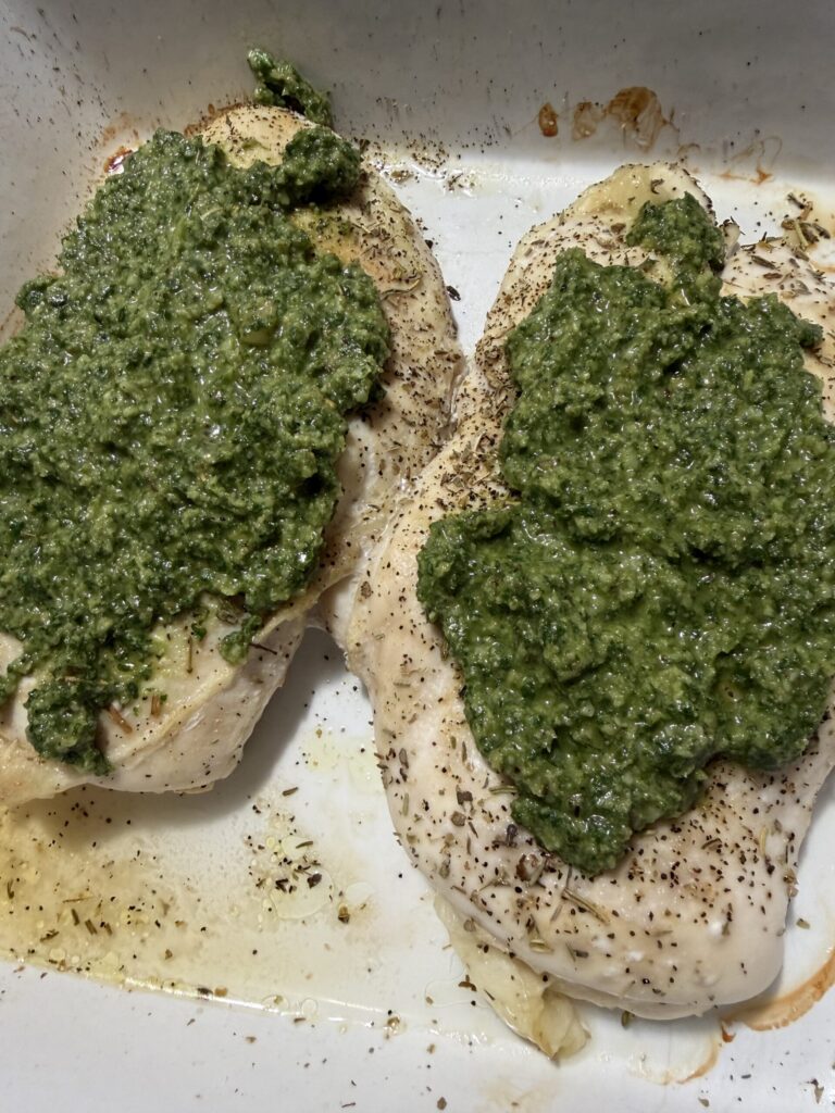 Homemade basil walnut pesto is spread over chicken breasts in a baking dish.