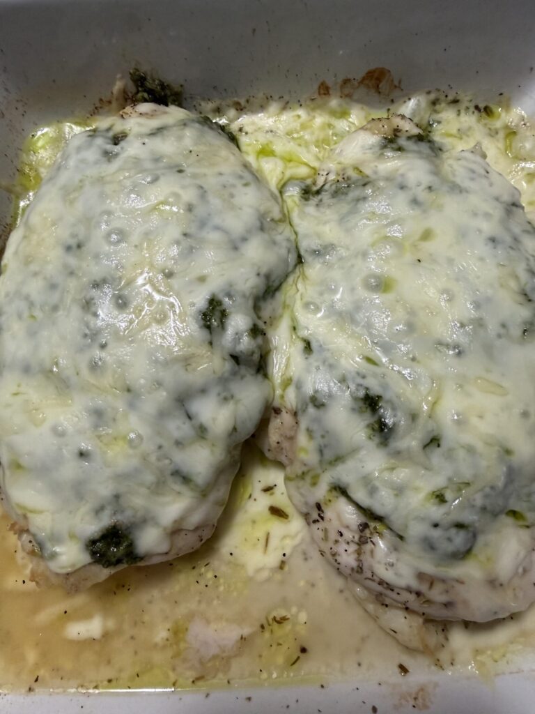 Melted cheeses and basil walnut pesto cover baked chicken ready to serve.