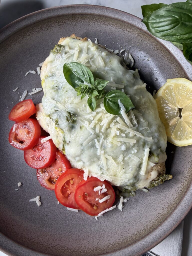Melted cheeses and fresh homemade pesto cover chicken creating a comforting dinner.