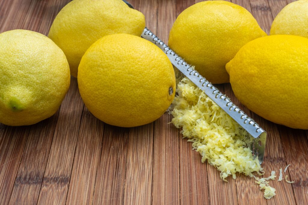 High angle of fresh ripe lemons and zest placed near grater on wooden table