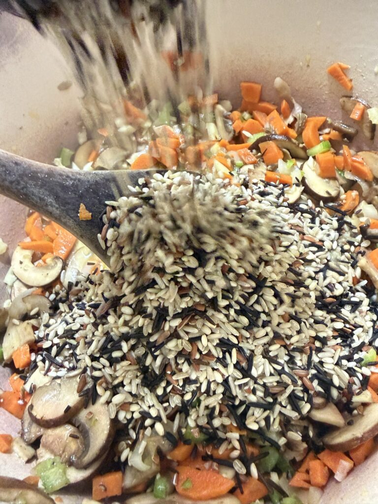 Wild Rice is being added to sautéed veggies to make creamy wild rice soup with rotisserie chicken