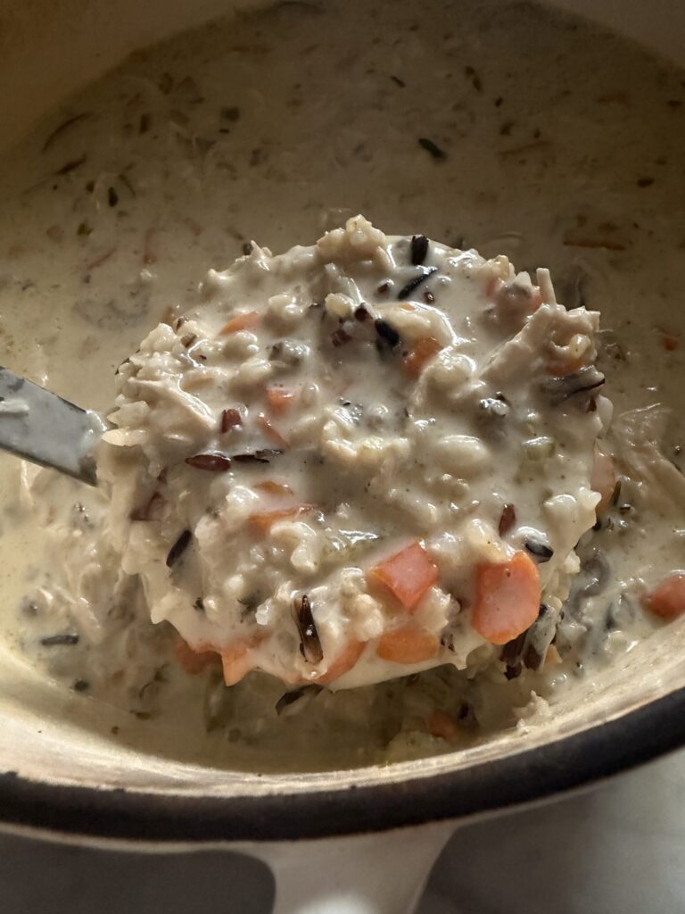 Ladling creamy wild rice and chicken soup to serve. 