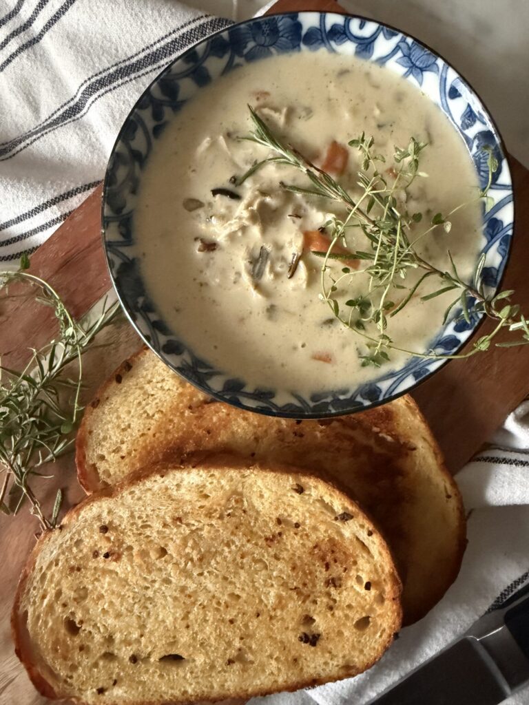 A bowl of creamy chicken and wild rice soup topped with fresh herbs and served with crusty sourdough bread