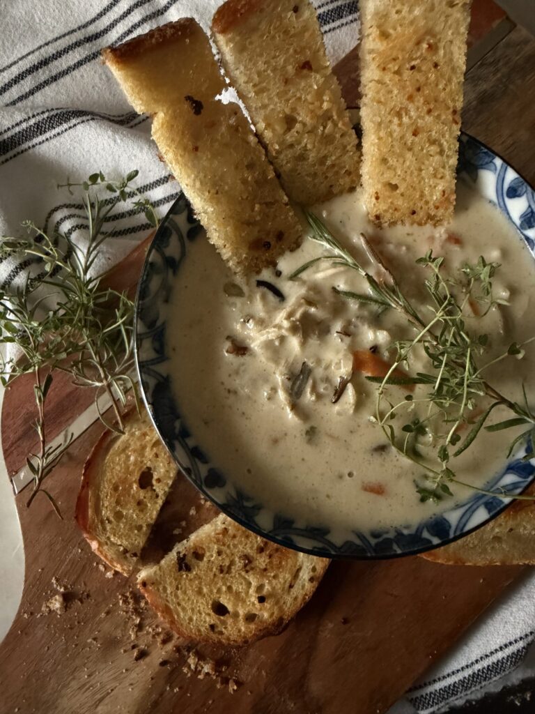 Creamy and cozy wild rice and chicken soup in a bowl with fresh herbs and crusty bread on a wooden surface
