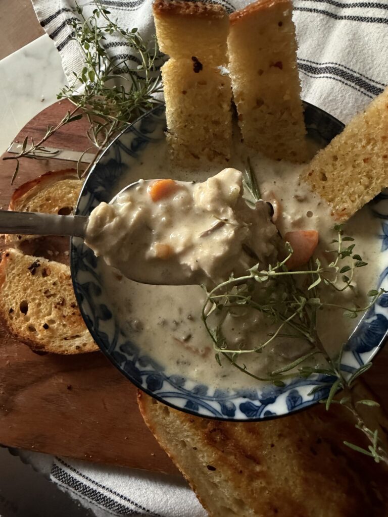 A spoonful of creamy wild rice soup with rotisserie chicken in a bowl served with fresh buttery sourdough garlic toast