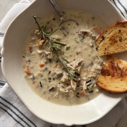 A hearty bowl of creamy wild rice and chicken soup on a striped tea towel served with crispy sourdough garlic toast