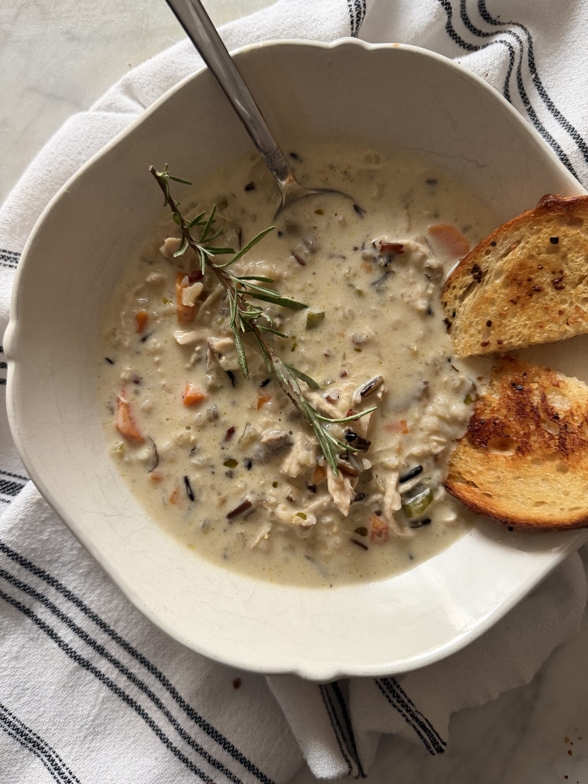 A hearty bowl of creamy wild rice and chicken soup on a striped tea towel served with crispy sourdough garlic toast
