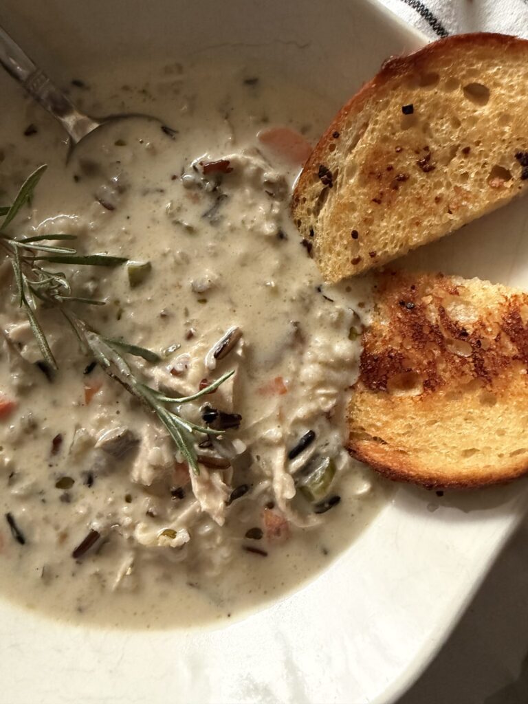 A creamy bowl of chicken and wild rice soup topped with fresh rosemary and served with butter sourdough garlic toast