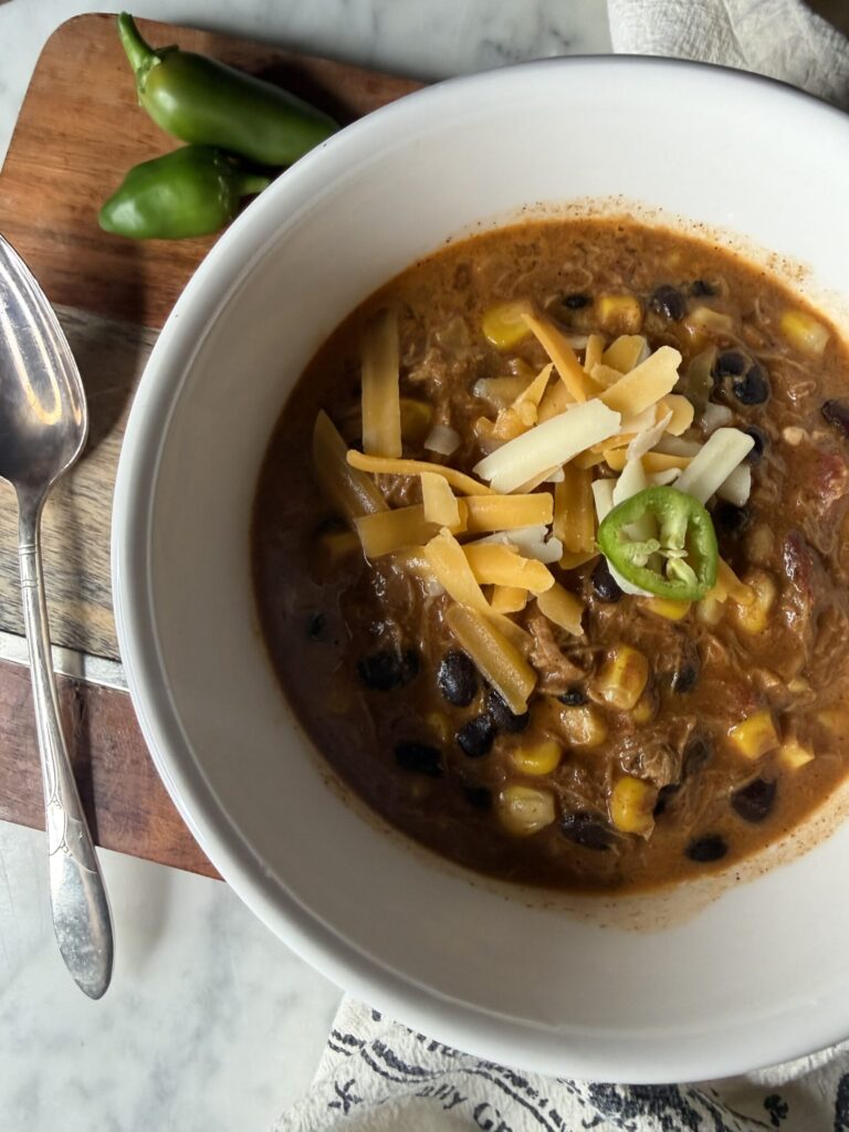 Warm chipotle chili with shredded cheese and jalapenos in a white bowl