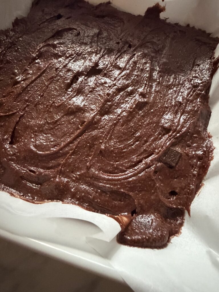 Brownie batter in a pan lined with parchment ready to bake.