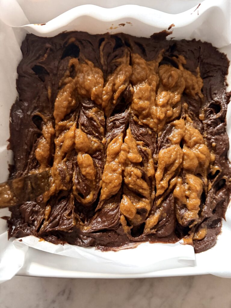 A butter knife is inserted into the brownie batter to make the swirl pattern of the pumpkin pie mixture.