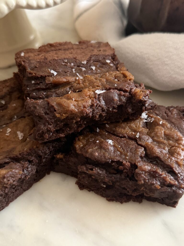 A stack of fudgy pumpkin swirl brownies with flaky sea salt on a marble surface ready to enjoy as a fall treat.