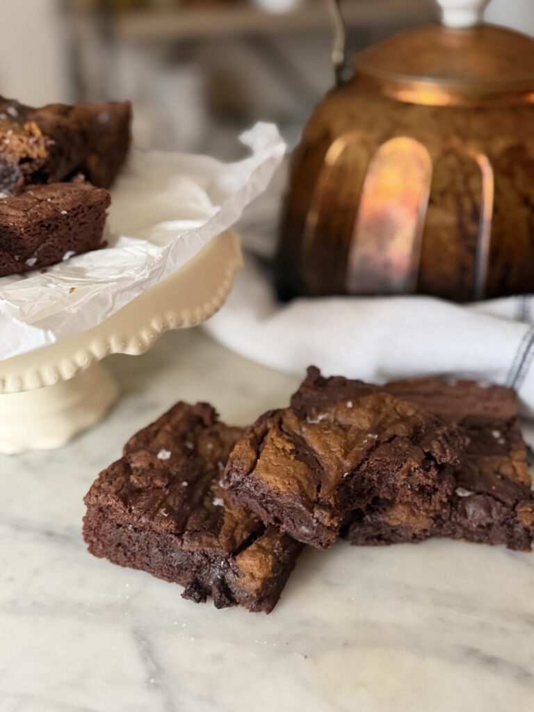 Three fudgy pumpkin swirl brownies on a marble surface with a decorative cake stand in the background.