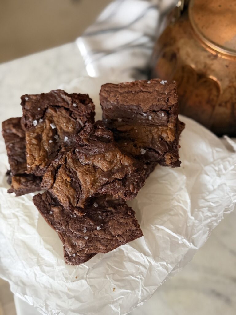 Pumpkin swirl brownies stacked on crinkled parchment paper with an antique copper kettle ready to serve as autumn treats.