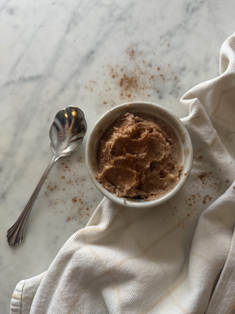 Creamy homemade cinnamon sugar honey butter in a white dish on a marble surface with a serving spoon and tea towel