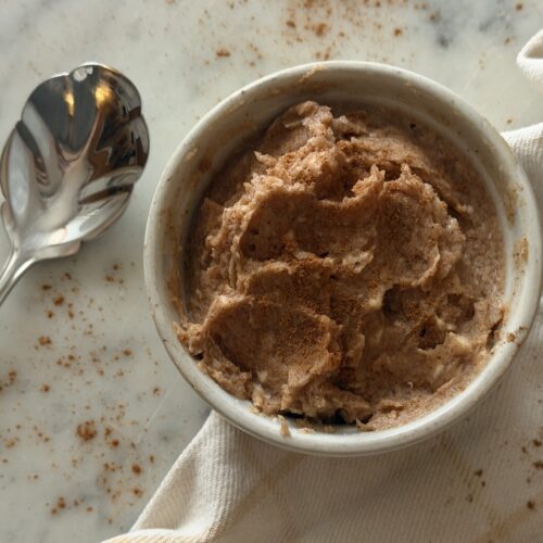 Creamy cinnamon sugar honey butter in a white dish with serving spoon topped with cinnamon