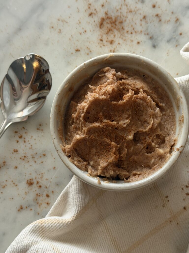 Creamy cinnamon sugar honey butter in a white dish with serving spoon topped with cinnamon