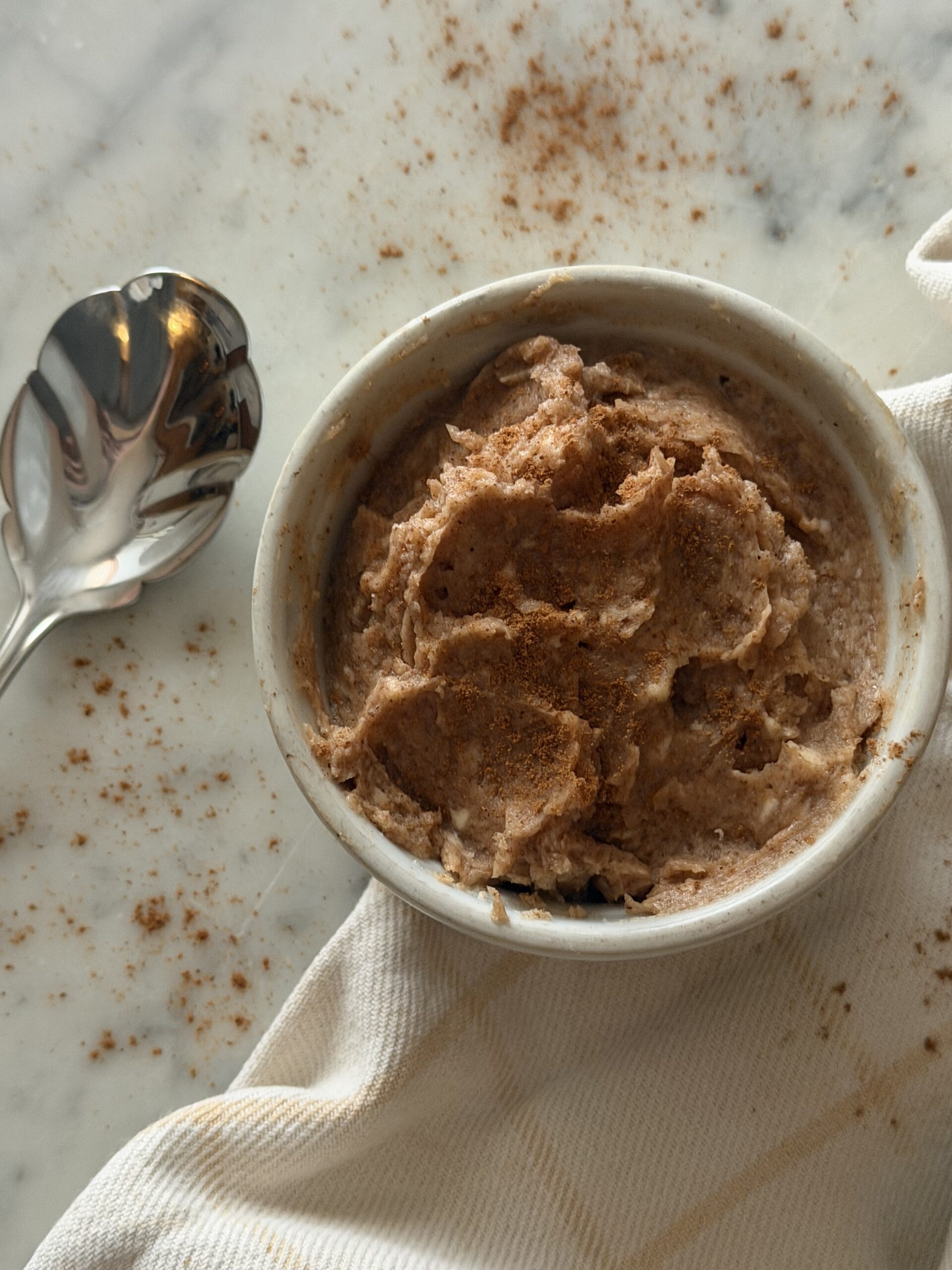 Creamy cinnamon sugar honey butter in a white dish with serving spoon topped with cinnamon