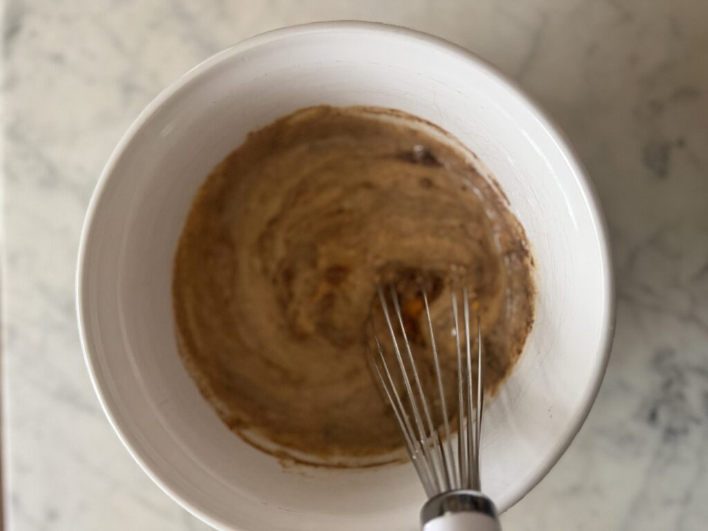 Ingredients for homemade pumpkin sauce are being whisked together in a white mixing bowl